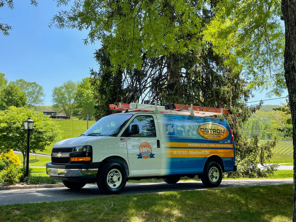 Ostrom service van parked on a driveway, shaded by trees. Green hills and blue sky in background.