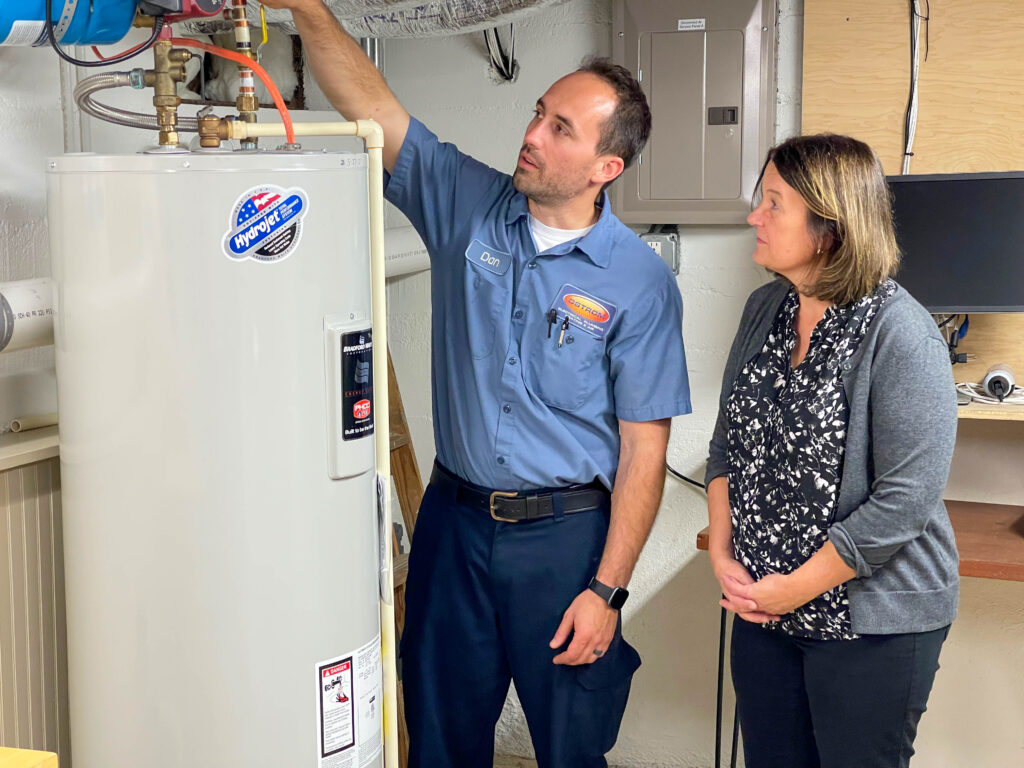 Ostrom plumber repairing a water heater while speaking with homeowner