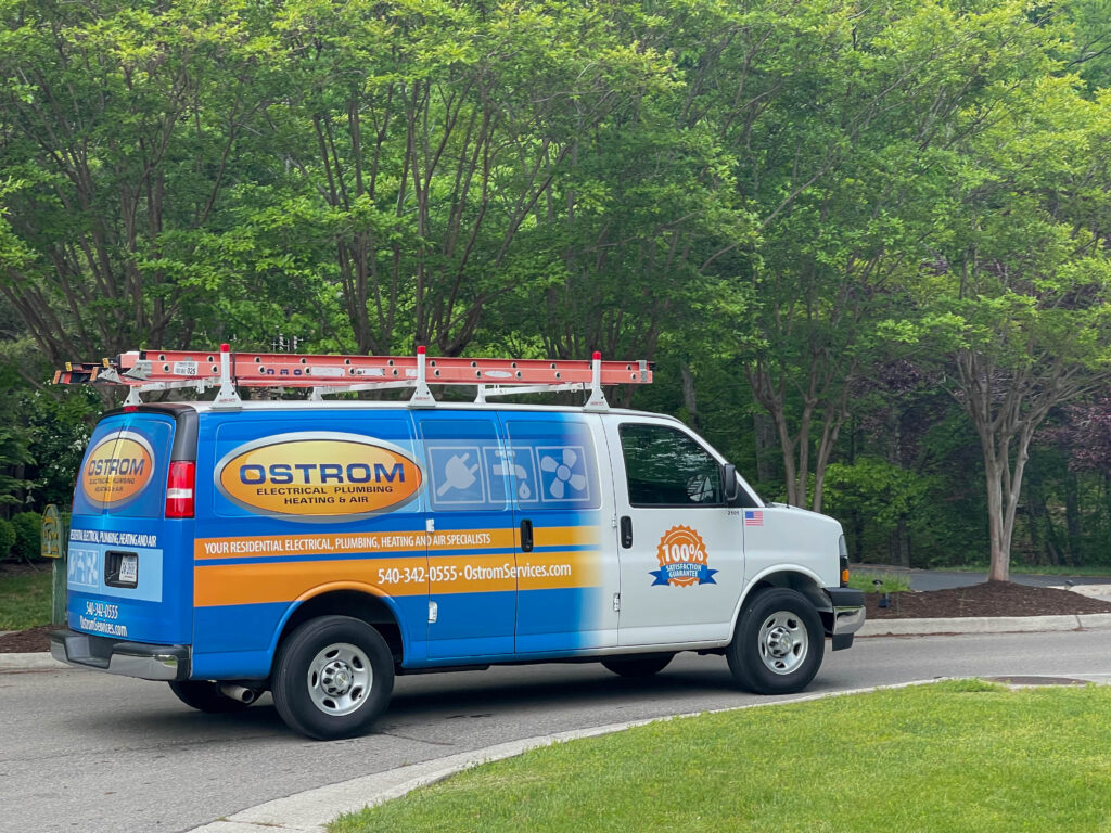 Ostrom plumbing service van parked on small road with green trees in background.