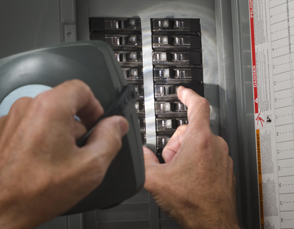 One hand holding a flash light while the other is flipping a circuit breaker on an electrical panel.