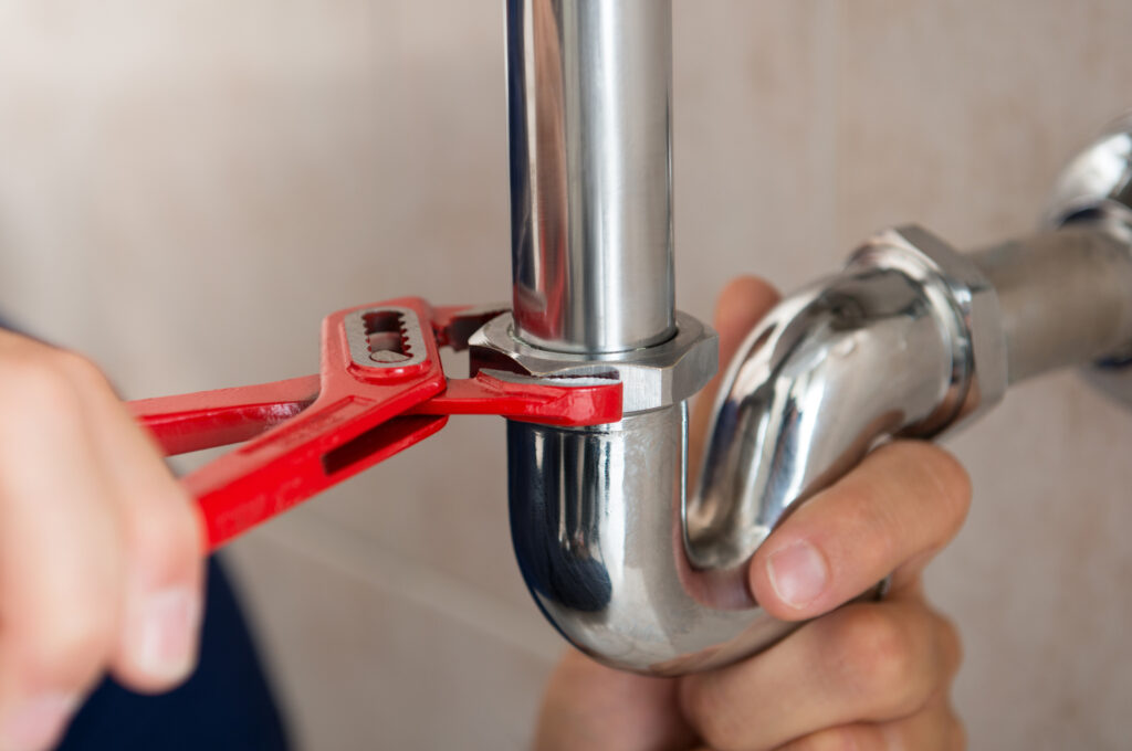Close-up of plumber repairing kitchen pipe with wrench 