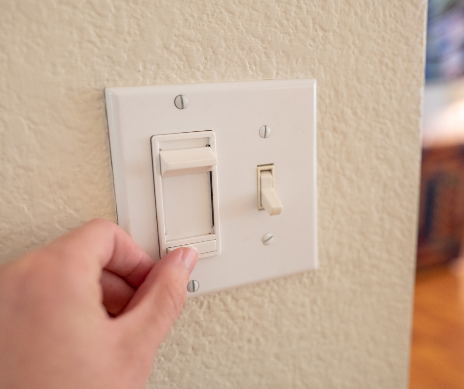 A close-up of a hand toggling a dimmer light switch, illustrating the action of switching the light on and off.